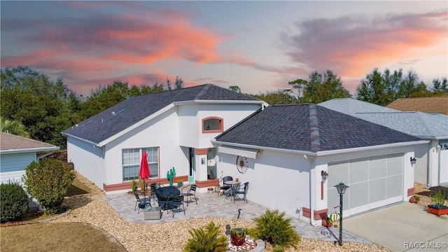 back house at dusk featuring a garage and a patio area