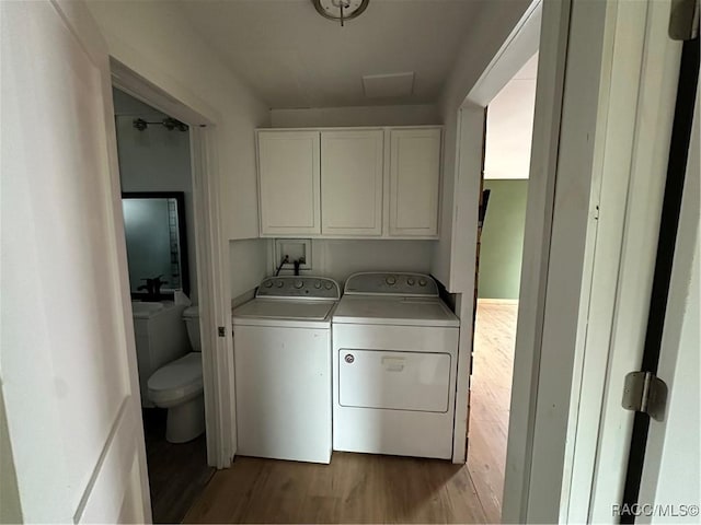 clothes washing area with cabinets, washer and clothes dryer, and light hardwood / wood-style flooring