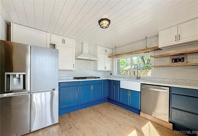 kitchen featuring wall chimney exhaust hood, blue cabinets, sink, white cabinetry, and stainless steel appliances