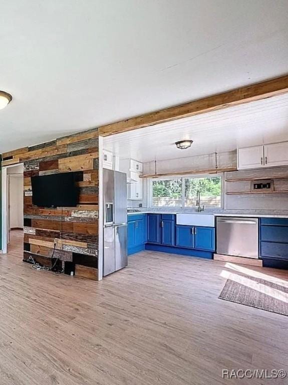 interior space featuring stainless steel appliances, blue cabinets, light hardwood / wood-style flooring, and wood walls