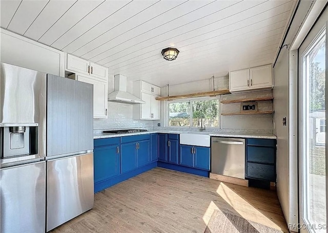 kitchen with wall chimney exhaust hood, appliances with stainless steel finishes, blue cabinets, and white cabinets