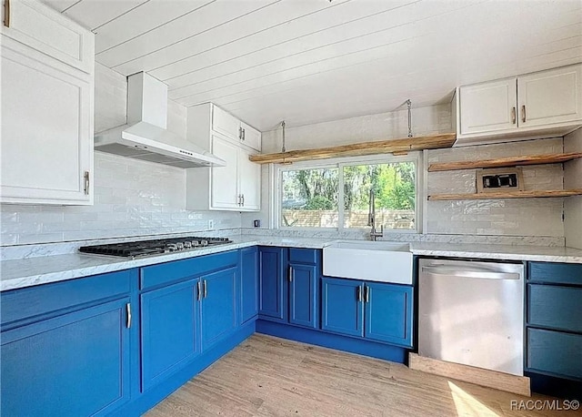 kitchen with blue cabinetry, white cabinetry, light hardwood / wood-style flooring, stainless steel appliances, and wall chimney range hood