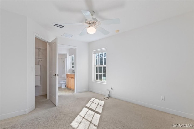 unfurnished bedroom featuring a closet, ensuite bath, light colored carpet, ceiling fan, and a spacious closet