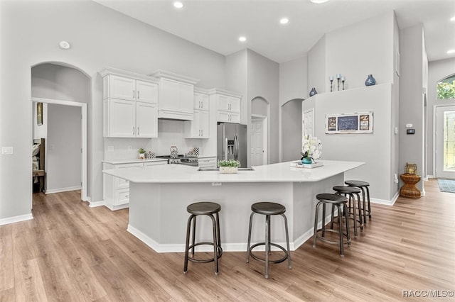 kitchen with light wood-type flooring, a spacious island, white cabinets, stainless steel fridge with ice dispenser, and a breakfast bar area