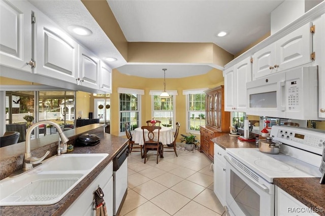 kitchen featuring light tile patterned flooring, white appliances, a sink, white cabinets, and dark countertops