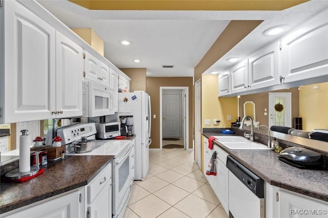 kitchen featuring dark countertops, white cabinets, a sink, light tile patterned flooring, and white appliances