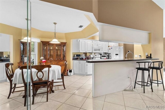 kitchen with a peninsula, white appliances, visible vents, dark countertops, and a kitchen bar