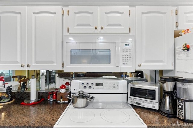 kitchen featuring dark countertops, white appliances, and white cabinets