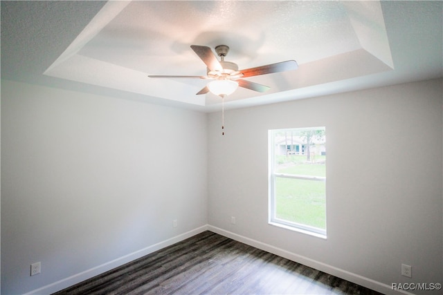 empty room featuring a raised ceiling, ceiling fan, and dark hardwood / wood-style flooring