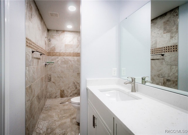 bathroom featuring a tile shower, vanity, and toilet