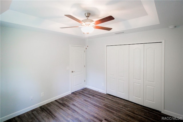 unfurnished bedroom featuring a raised ceiling, ceiling fan, a closet, and dark wood-type flooring