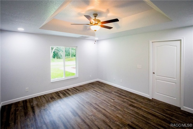 unfurnished room with ceiling fan, dark hardwood / wood-style flooring, a textured ceiling, and a tray ceiling