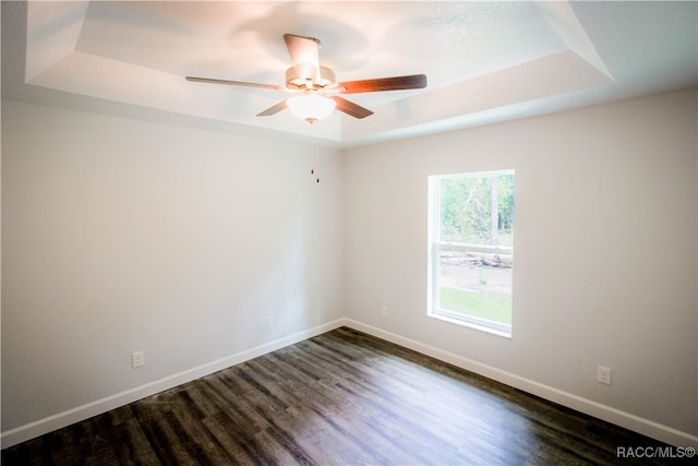 empty room featuring dark hardwood / wood-style floors, ceiling fan, and a raised ceiling