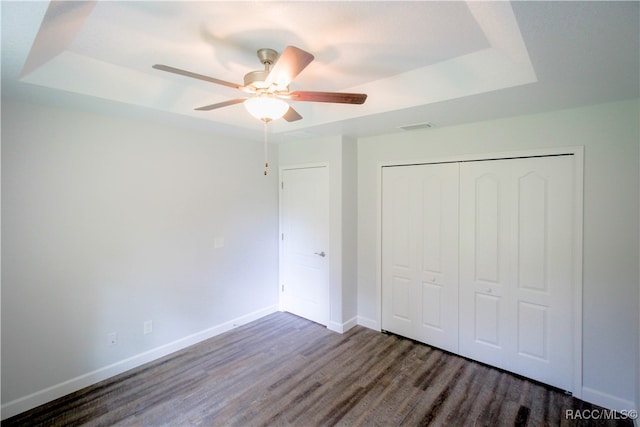 unfurnished bedroom with a closet, ceiling fan, dark wood-type flooring, and a tray ceiling