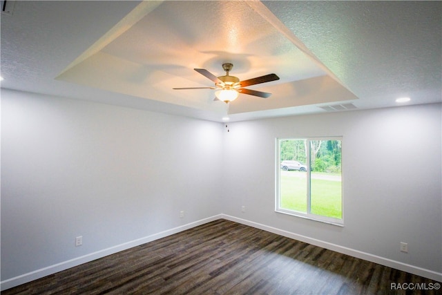 empty room with a tray ceiling, ceiling fan, dark hardwood / wood-style flooring, and a textured ceiling