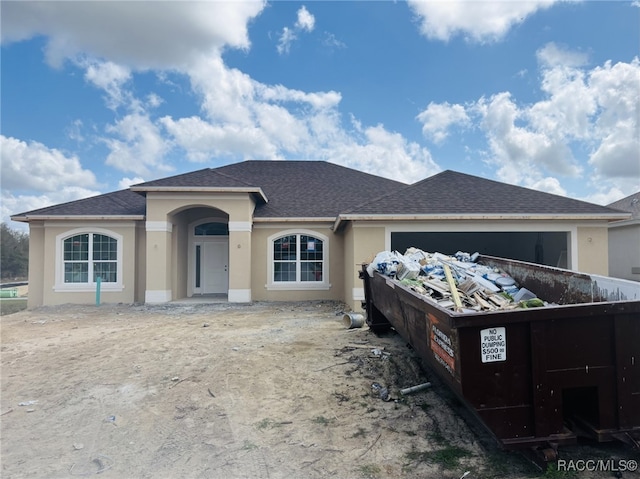 ranch-style home featuring stucco siding and roof with shingles