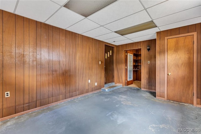 unfurnished room with concrete flooring, a drop ceiling, and wood walls