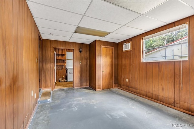 unfurnished room with a drop ceiling, a wall mounted AC, and wood walls