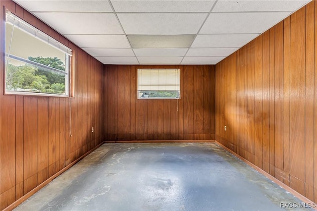 unfurnished room with wooden walls, a paneled ceiling, and concrete flooring