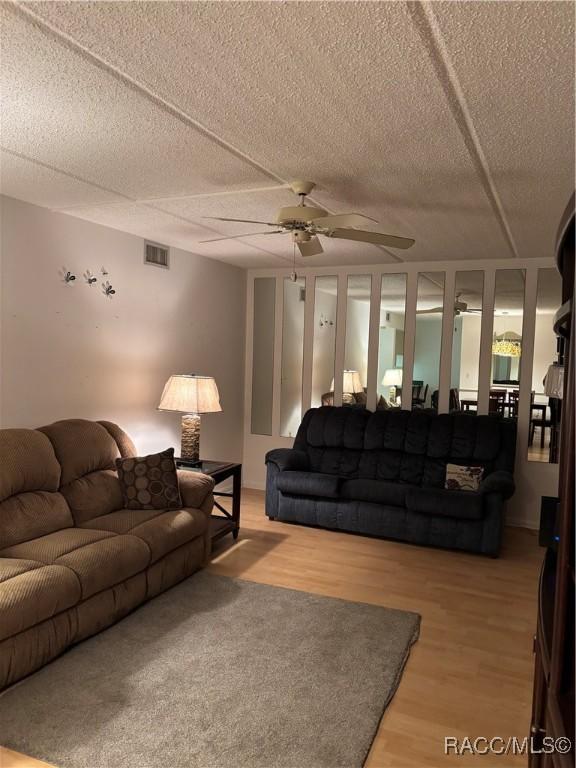 living room featuring light hardwood / wood-style floors, a textured ceiling, and ceiling fan