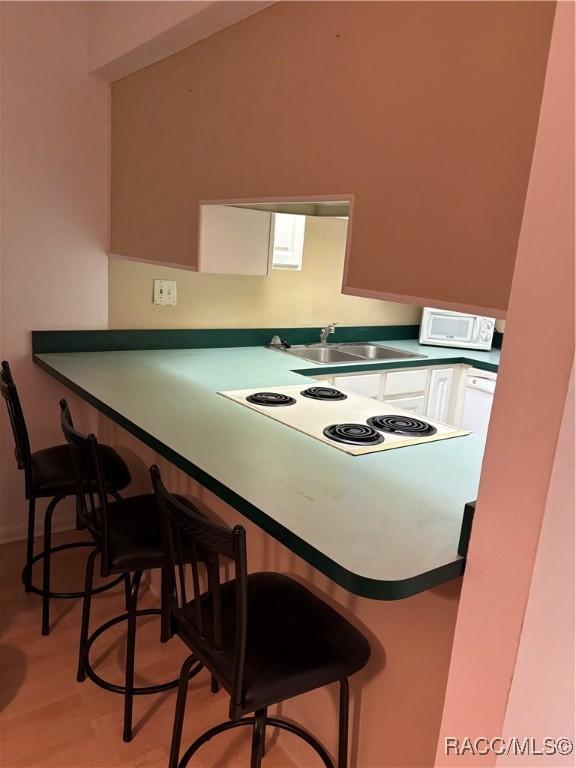 kitchen featuring white cabinets, a kitchen bar, sink, and light hardwood / wood-style flooring