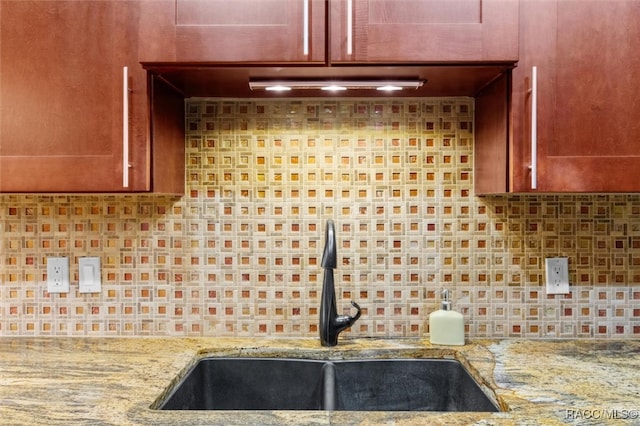 kitchen with decorative backsplash, light stone countertops, and sink