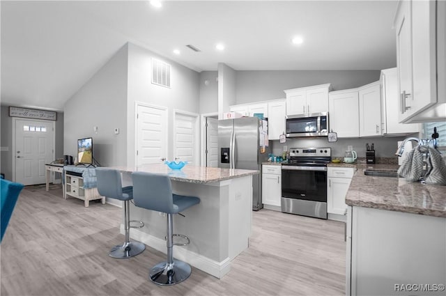 kitchen with stainless steel appliances, a center island, sink, light stone counters, and white cabinets