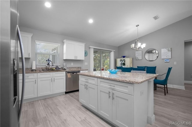 kitchen with appliances with stainless steel finishes, lofted ceiling, decorative light fixtures, a kitchen island, and white cabinetry