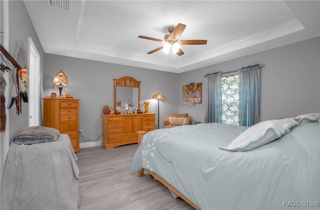 bedroom featuring a closet, ceiling fan, a tray ceiling, ornamental molding, and light wood-type flooring