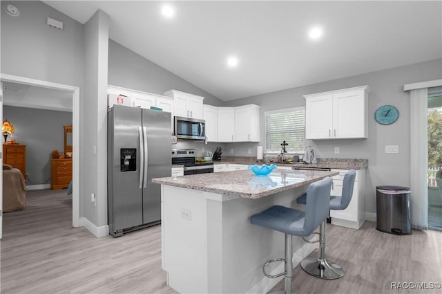 kitchen with a kitchen breakfast bar, a kitchen island, stainless steel appliances, and white cabinetry