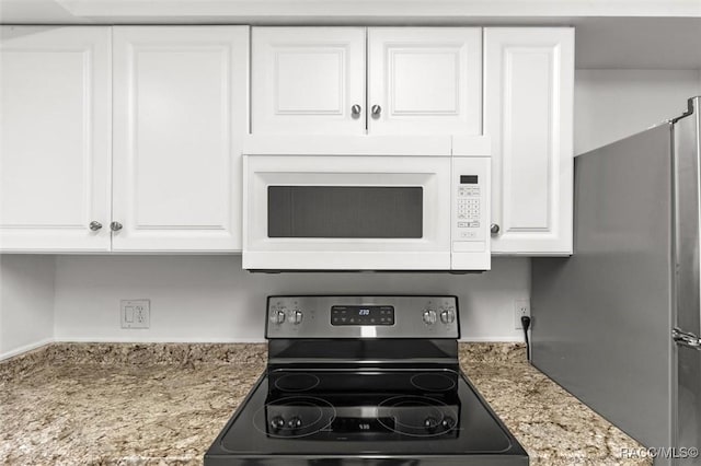 kitchen with electric stove, white microwave, freestanding refrigerator, white cabinetry, and light stone countertops