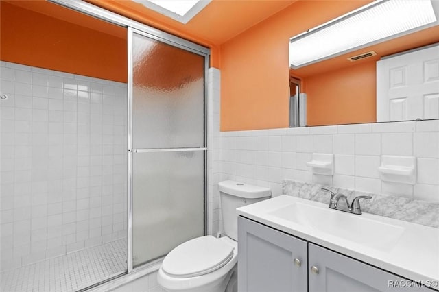 full bath with toilet, visible vents, vanity, tile walls, and a tile shower