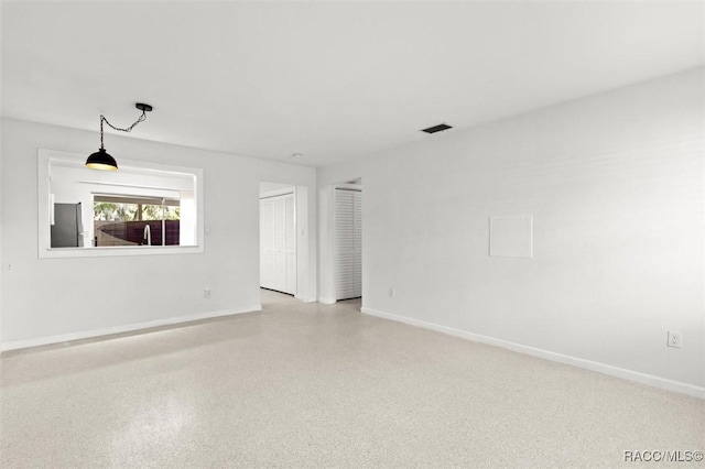 empty room featuring light speckled floor, visible vents, and baseboards