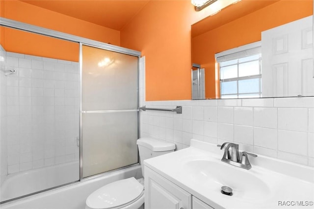 full bathroom with a wainscoted wall, shower / bath combination with glass door, tile walls, toilet, and vanity