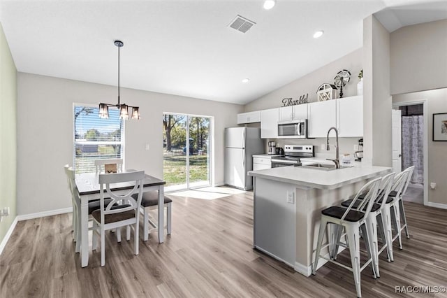 kitchen featuring light wood-style flooring, a sink, visible vents, vaulted ceiling, and appliances with stainless steel finishes