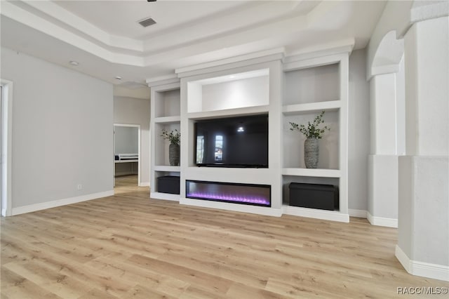 unfurnished living room with built in shelves, a raised ceiling, and light hardwood / wood-style flooring