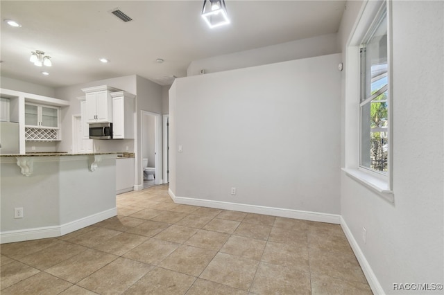 kitchen with kitchen peninsula, a breakfast bar, light tile patterned floors, stone counters, and white cabinets