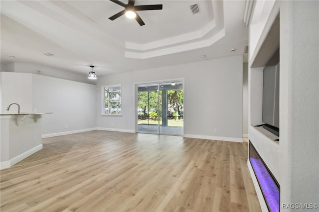 unfurnished living room with light wood-type flooring, a tray ceiling, ceiling fan, and sink