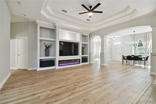 unfurnished living room featuring a tray ceiling, built in features, and light hardwood / wood-style floors