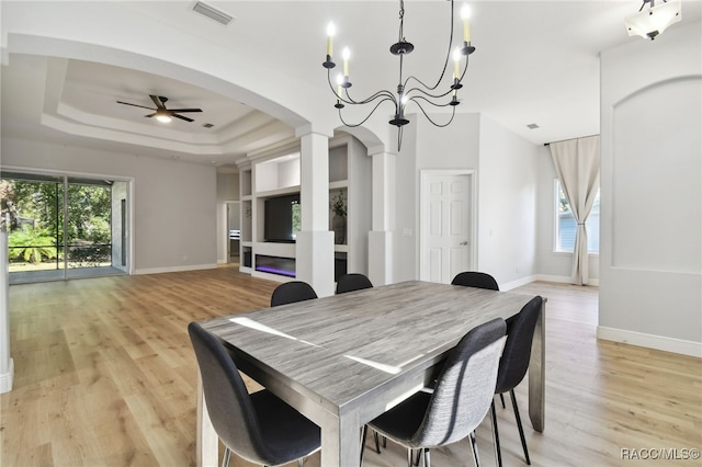 dining area featuring ceiling fan with notable chandelier, light wood-type flooring, and a tray ceiling