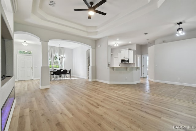 unfurnished living room featuring ceiling fan with notable chandelier, light wood-type flooring, and a tray ceiling