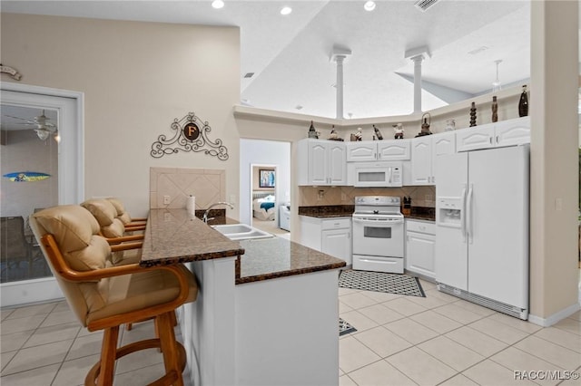 kitchen featuring white appliances, light tile patterned floors, a peninsula, a sink, and white cabinetry