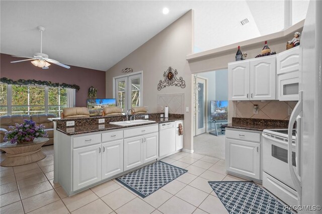 kitchen with a sink, dark stone counters, white appliances, a peninsula, and white cabinets