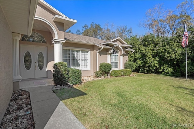 doorway to property with stucco siding, a lawn, and roof with shingles