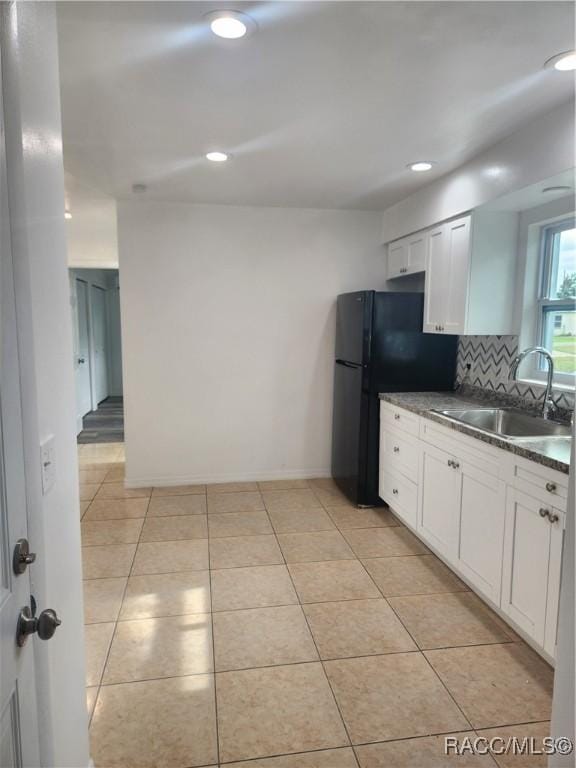 kitchen featuring black refrigerator, backsplash, sink, white cabinets, and light tile patterned flooring