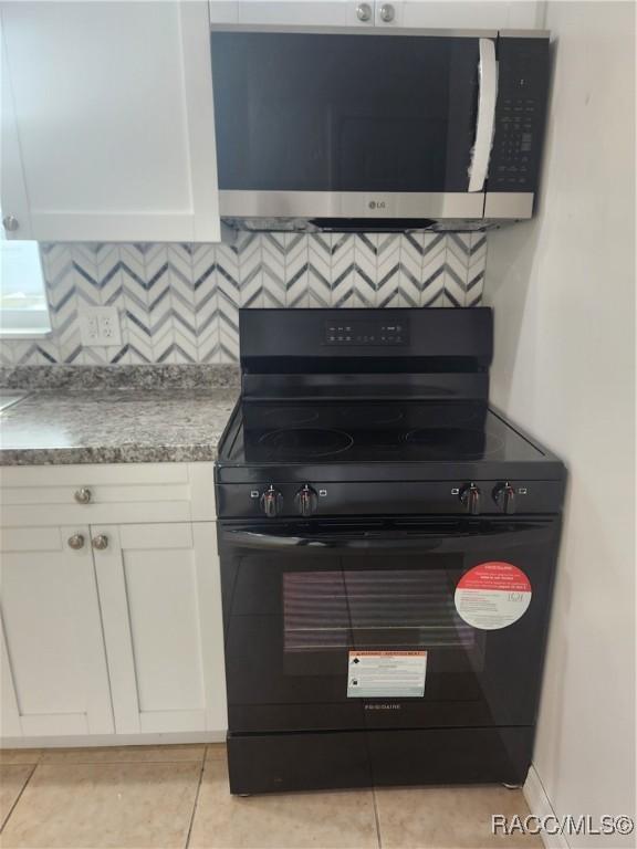 kitchen with decorative backsplash, black range with gas stovetop, white cabinetry, and light tile patterned floors