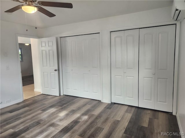 unfurnished bedroom with two closets, an AC wall unit, ceiling fan, and dark wood-type flooring