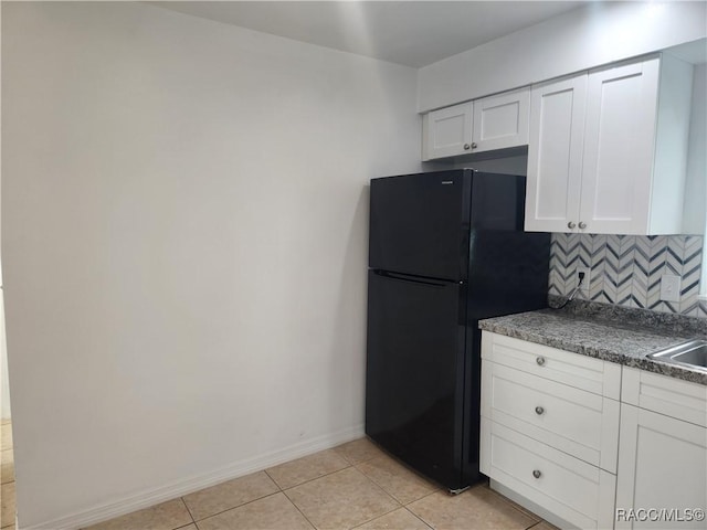 kitchen featuring black refrigerator, decorative backsplash, sink, white cabinetry, and light tile patterned flooring