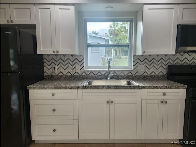 kitchen featuring tasteful backsplash, black fridge, sink, white cabinets, and range