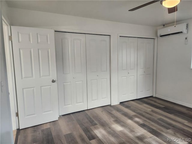 unfurnished bedroom featuring ceiling fan, an AC wall unit, dark wood-type flooring, and multiple closets